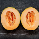 Two halves of a Hale’s Best Jumbo cantaloupe showing thick orange flesh and seeds on a dark marble surface.