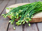 Freshly harvested Garlic Chives with green stems and unopened flower buds resting on a wooden cutting board.