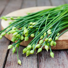 Freshly harvested Garlic Chives with green stems and unopened flower buds resting on a wooden cutting board.