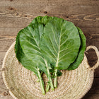 Freshly harvested Georgia Southern collard greens in a woven basket on a rustic wooden table.