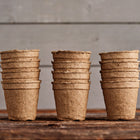 Three stacks of brown, 3-inch round CowPots made from composted manure on a rustic wooden surface.