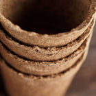 A stack of three-inch round CowPots made from brown, fibrous composted cow manure on a dark wooden surface.