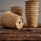 Stacked 3-inch round CowPots made of brown, textured composted manure on a rustic wooden surface.