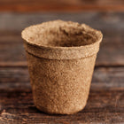 Empty 3-inch round CowPots biodegradable garden pot made of composted manure on a wooden surface.