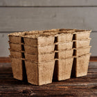 Stack of brown, biodegradable 3-inch six-cell CowPots made from composted manure on a rustic wooden surface.