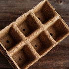 Empty 3-inch six-cell CowPots made of brown, fibrous composted manure on a rustic wooden surface.