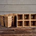 Stacked 3-inch six-cell CowPots made of brown, textured composted manure on a rustic wooden surface.
