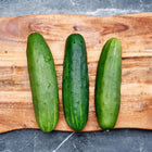 Three dark green Marketmore 76 cucumbers with water droplets resting on a wooden cutting board.