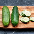Two whole Marketmore 76 cucumbers and several fresh slices on a wooden cutting board.