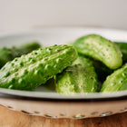 Freshly harvested, knobby green Parisian Pickling cucumbers piled in a white enameled colander.