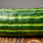 Close-up of a Striped Armenian cucumber showing ribbed, pale and dark green striped skin on a wooden surface.