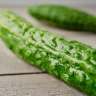 Two long, slender, and ribbed Suyo Long cucumbers resting on a grey wooden surface.