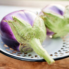 Two round Rosa Bianca eggplants with lavender and white skin resting on a white decorative metal plate.