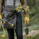 Barebones Garden Trowel with a stainless steel blade and wooden handle held by a person wearing yellow leather gloves.