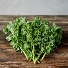 Freshly harvested Blue Curled Scotch kale with ruffled, blue-green leaves resting on a rustic wooden surface.