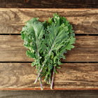 Freshly harvested Red Russian kale with frilled green leaves and purple stems resting on a rustic wooden crate.