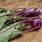 Freshly harvested Purple Vienna kohlrabi with vibrant violet bulbs and green leaves on a rustic wooden surface.