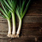 Three harvested American Flag leeks with white stems and green leaves on a rustic dark wooden surface.