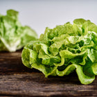 Two fresh, tender heads of Tom Thumb butterhead lettuce resting on a rustic wooden surface.