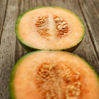 Two halves of a sliced Charentais melon showing salmon-orange flesh and seeds on a rustic wooden surface.