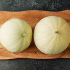 Two round Tam Dew honeydew melons with creamy yellow rinds resting on a wooden cutting board.