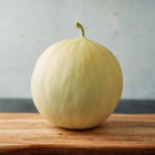 A whole Tam Dew honeydew melon with a smooth, creamy yellow rind sitting on a wooden cutting board.