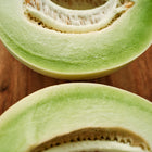 Two halves of a sliced Tam Dew melon showing pale green flesh and seeds on a wooden cutting board.