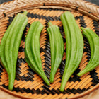 Freshly harvested Clemson Spineless okra pods arranged on a round, woven bamboo tray.