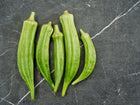 Five fresh, green Clemson Spineless okra pods arranged vertically on a dark grey marble surface.
