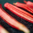 Slender, vibrant orange-red Jing Orange okra pods arranged on a dark, textured surface.