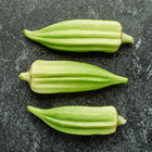 Three Star of David okra pods with thick, green, ribbed skin arranged horizontally on a dark, textured surface.