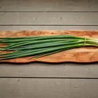 A bunch of Evergreen Bunching onions with long green tops and white shanks resting on a rustic wooden board.