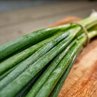 A bunch of fresh Evergreen Bunching onions with green stalks and white shanks tied with twine on a wooden cutting board.