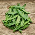 A pile of freshly harvested Laxton’s Progress #9 pea pods resting on a rustic wooden surface.