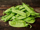 A pile of fresh, light green Mammoth Melting Sugar snow pea pods resting on a rustic dark wooden surface.