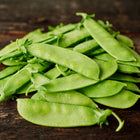 A pile of fresh, light green Mammoth Melting Sugar snow pea pods resting on a rustic dark wooden surface.