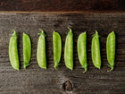 Freshly harvested Mammoth Melting Sugar snow pea pods lined up horizontally on a rustic dark wooden surface.