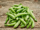 A pile of fresh, dew-covered Sugar Ann snap pea pods resting on a rustic wooden surface.