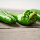 Three long, smooth green Anaheim peppers resting on a weathered wooden surface.