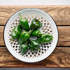 Fresh dark green Poblano peppers arranged on a white decorative metal plate atop a rustic wooden crate.