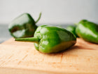 Fresh dark green Poblano peppers resting on a wooden cutting board.