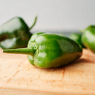 Fresh dark green Poblano peppers resting on a wooden cutting board.