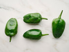 Four dark green, heart-shaped Poblano peppers arranged on a white marble surface.