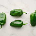 Four dark green, heart-shaped Poblano peppers arranged on a white marble surface.