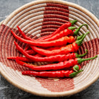 Bright red Cayenne Long Slim peppers in a woven, patterned basket on a dark marble surface.