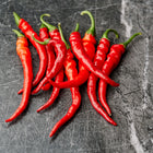A cluster of slender, bright red Cayenne Long Slim peppers with green stems resting on a dark gray marble surface.