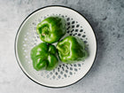 Three glossy green Emerald Giant bell peppers arranged on a decorative white and grey patterned plate.