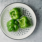 Three glossy green Emerald Giant bell peppers arranged on a decorative white and grey patterned plate.
