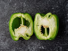 Two halves of a sliced Emerald Giant green bell pepper showing thick walls and seeds on a dark textured background.