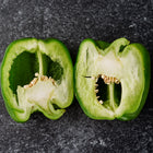 Two halves of a sliced Emerald Giant green bell pepper showing thick walls and seeds on a dark textured background.